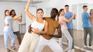 Group of excited young adult people dancing dynamic moves in pairs during lesson in dance class