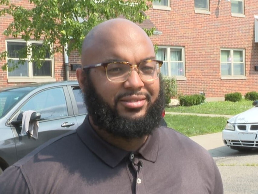 Carlton Collins is wearing a gray shirt in this photo. He has a beard and mustache and a shaved head.