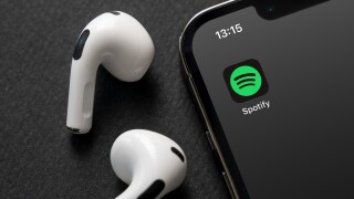 Spotify logo on a phone next to airpods.