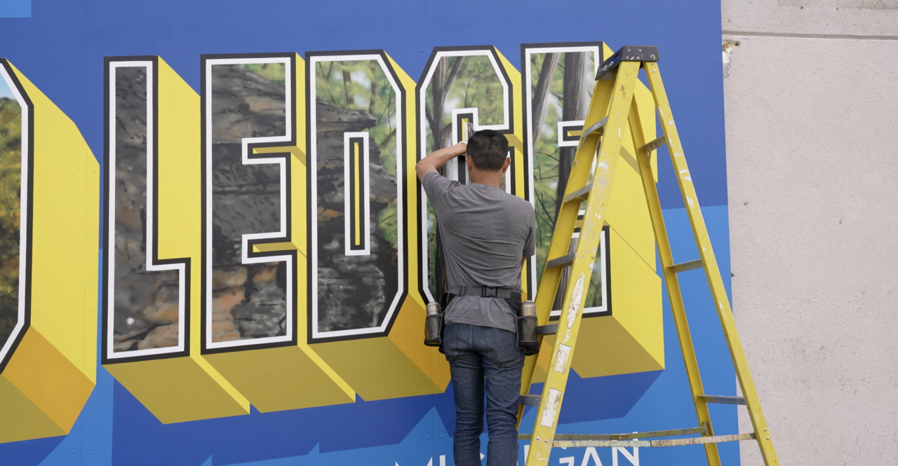 Victor Ving is working on the mural in Grand Ledge