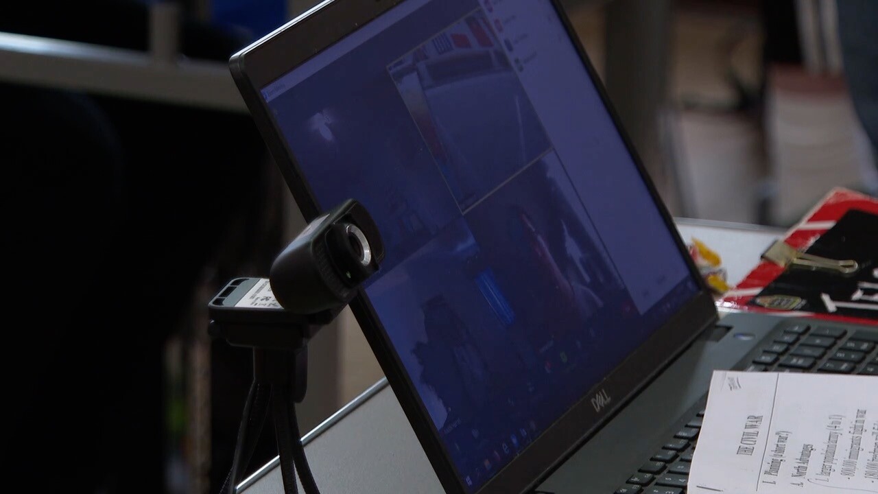 A laptop equipped with a webcam sits on a teacher's desk.