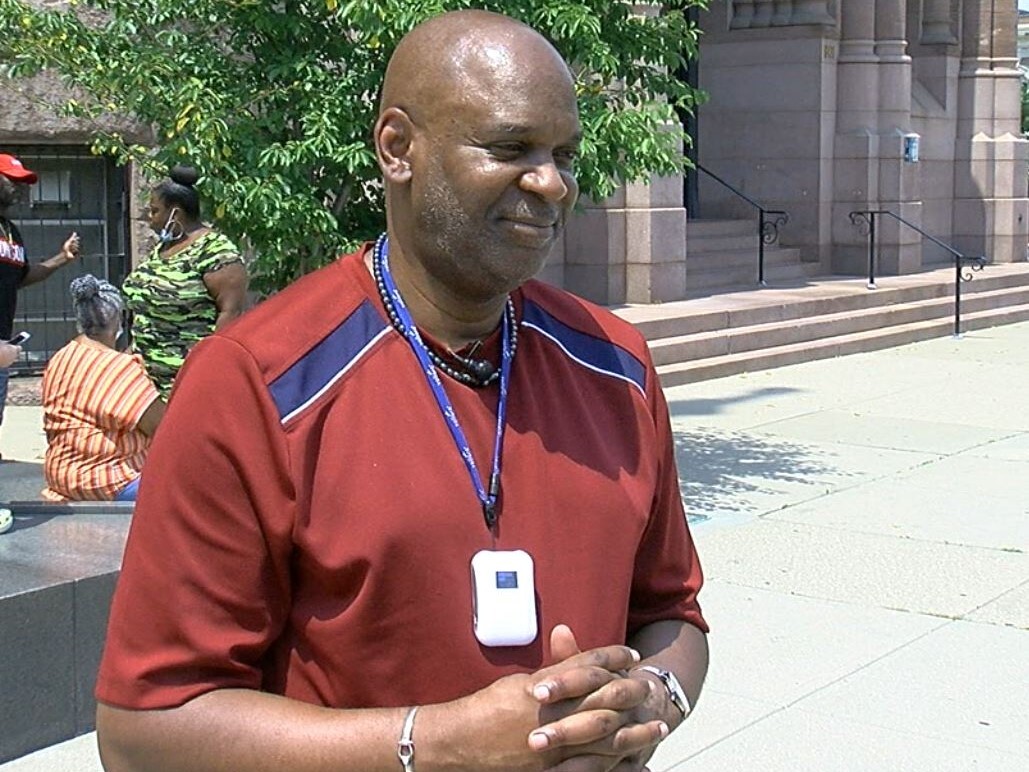 This is a photo of the Rev. Damon Lynch standing outside Cincinnati City Hall. His head is shaved, and he has a very close cropped beard and mustache.