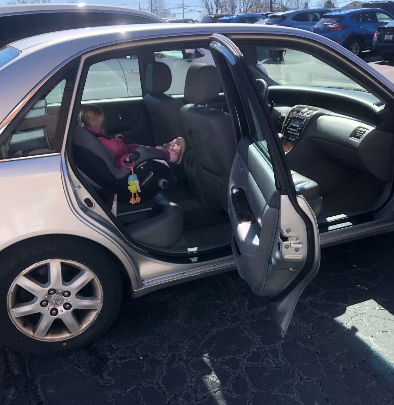 A child sits buckled into a car seat in the back of a 2000 Toyota Avalon. The child's face is blurred for privacy.