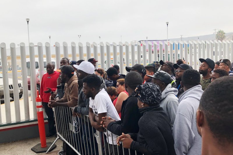 In this Sunday, July 28, 2019, photo, migrants in Tijuana, many from Cameroon, listen to names being called for those who can claim asylum that day in the US. English-speaking Cameroonians fleeing atrocities of their French-speaking government helped push Tijuana’s asylum wait list to 10,000 on Sunday, up from 4,800 just three months earlier. (AP Photo/Elliot Spagat)