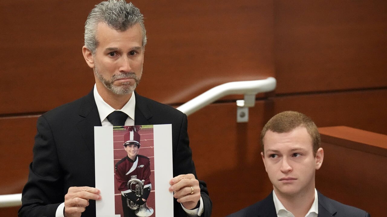 Max Schachter, with his son, Ryan, by his side, holds a photograph of his other son, Alex, just before giving his victim impact statement during the penalty phase of the trial of Marjory Stoneman Douglas High School shooter Nikolas Cruz at the Broward County Courthouse in Fort Lauderdale, Fla., Wednesday, Aug. 3, 2022. Alex Schachter was killed in the 2018 shootings. 