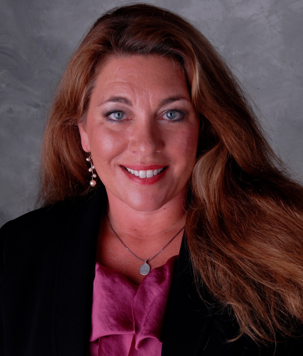 Jeanne Golliher is smiling in this photo. She has blue eyes, long, wavy brown hair and is wearing a mauve blouse and black jacket.