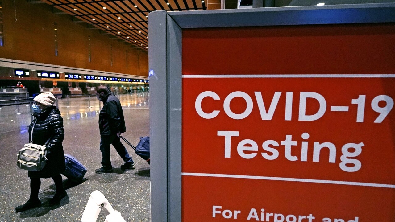 Travelers pass a sign near a COVID-19 testing site