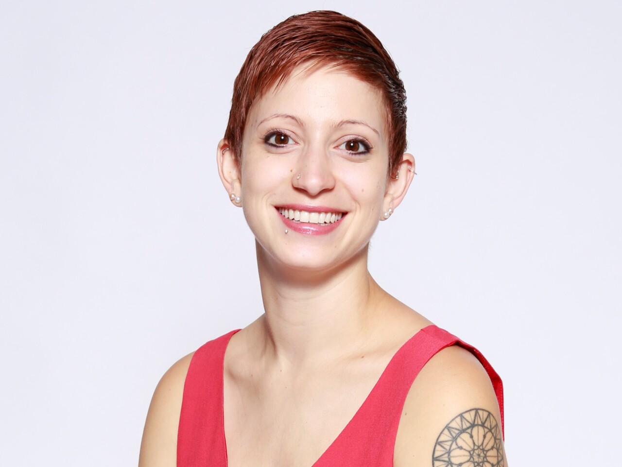 Marie Krulewitch-Browne is smiling in this photo. She has short-cropped red hair and is wearing a red, sleeveless top.