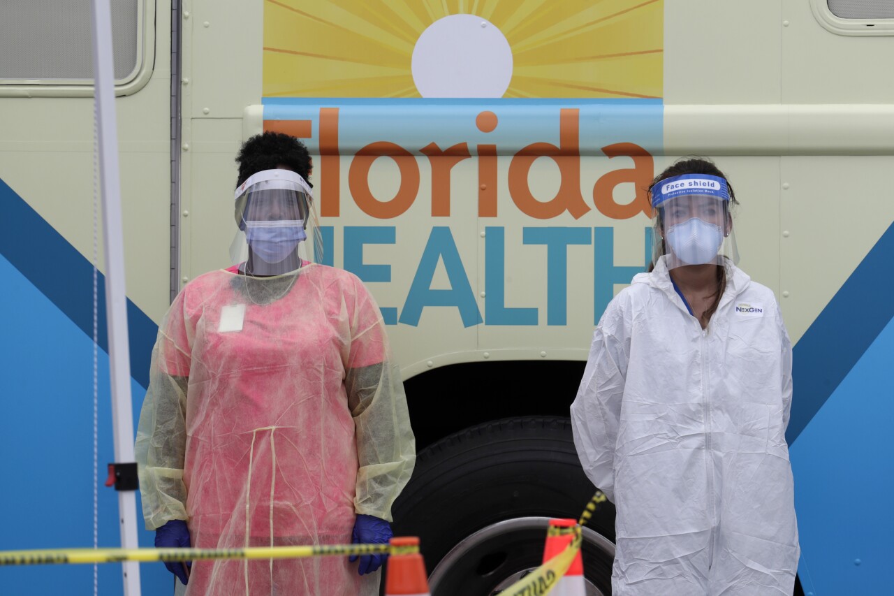 Health workers wearing protective gear in front of mobile coronavirus testing lab