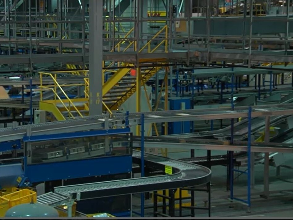 This photo shows the inside of DHL Express operations with many levels of conveyor belts and stairs.