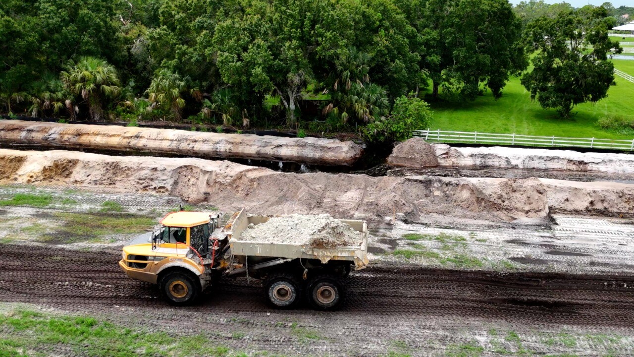 Dump truck moving dirt in front of the unblocked drainage ditch.
