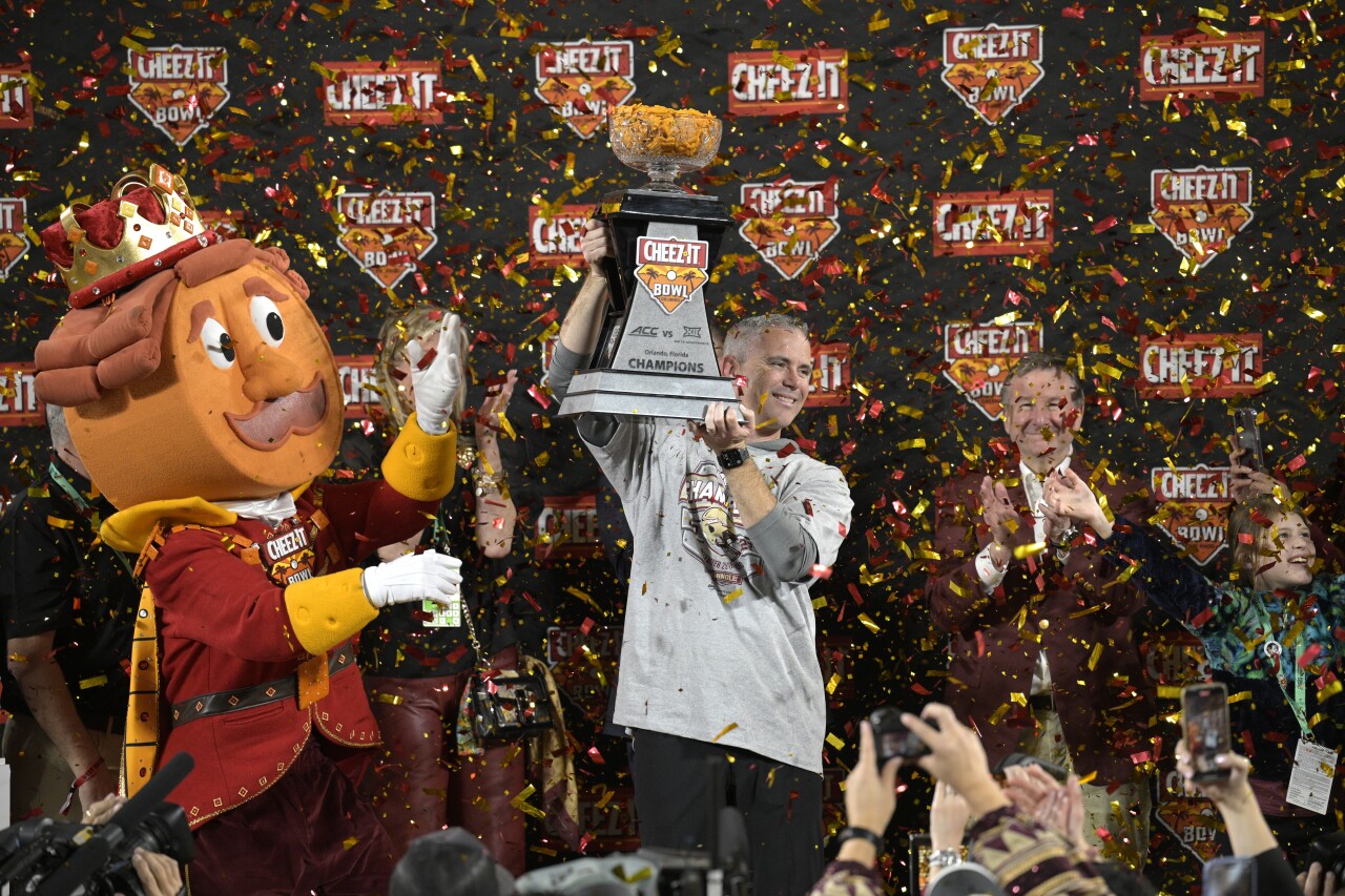 Florida State Seminoles head coach Mike Norvell lifts 2022 Cheez-It Bowl trophy while standing next to Cheez-It Bowl mascot