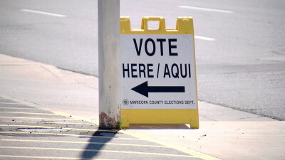 A "vote here/aqui" sign sits on a sidewalk in Maricopa County.