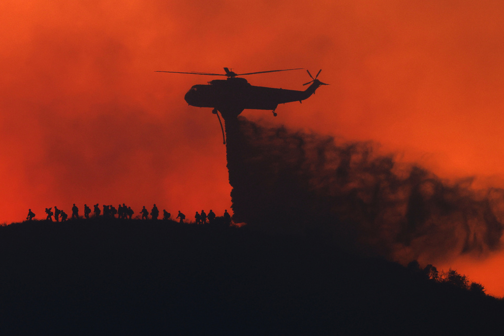 A water tanker drops water while firefighters walk below, as the Sandy Fire approaches, Tuesday, May 19, 2026, in Simi Valley, Calif.