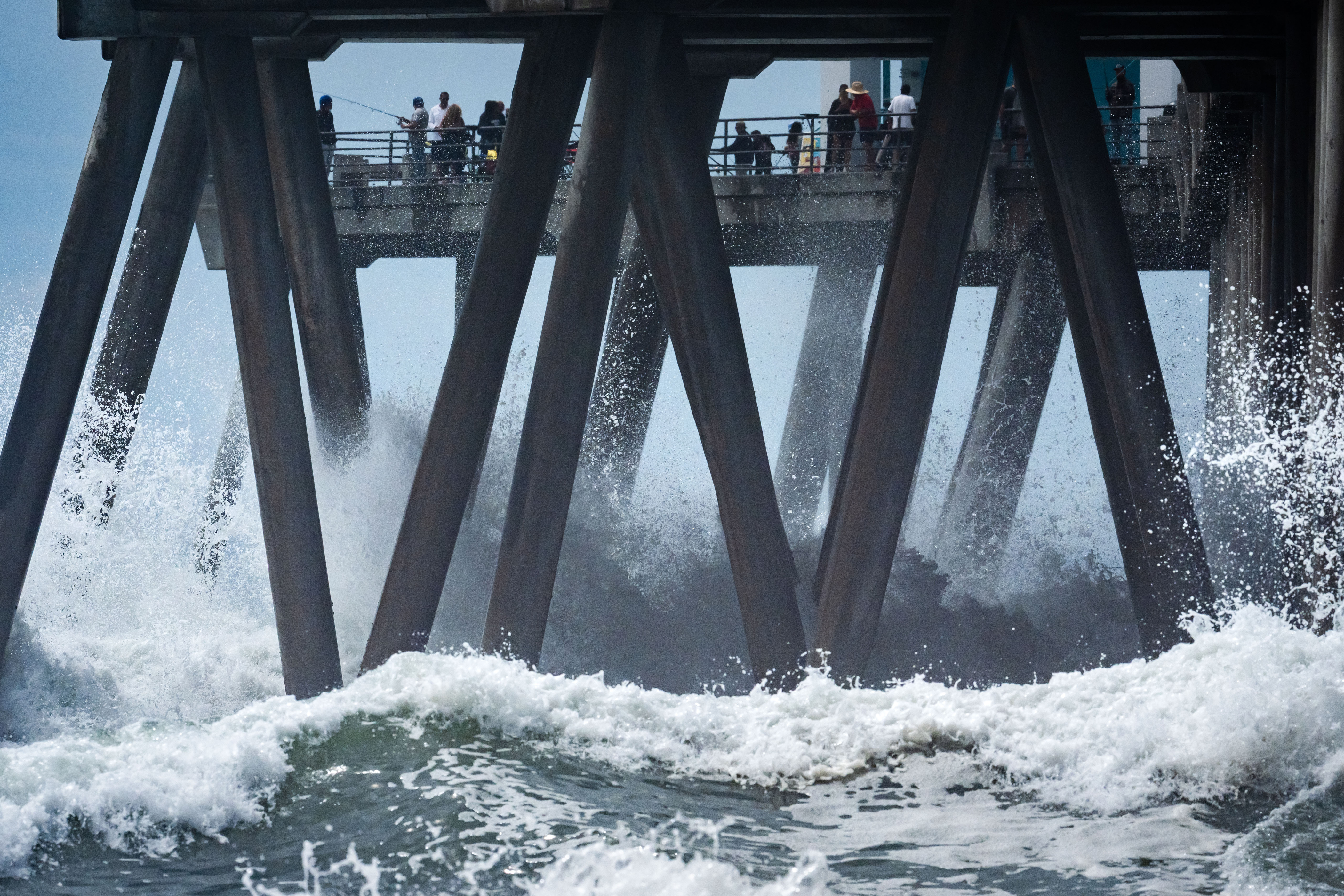 People walk on a pier as large waves from Hurricane Marie break on the shore, Monday, Sept. 7, 2026, on Huntington Beach, southern Calif.