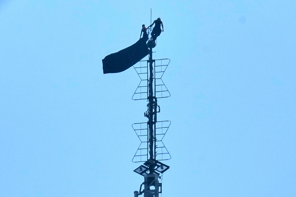 Two people stand on the tip of the antenna of the Empire State Building while holding a banner on Wednesday, July 1, 2026. 