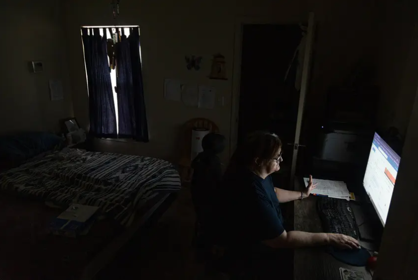 Terri Rimmer uses her computer to search for remote jobs in her Fort Worth apartment on Sept. 9, 2023. A blackout curtain on the window helps keep the room cool. Rimmer said the trauma from the February 2021 winter storm caused her to shut off her air conditioning last summer when the state grid operator asked Texans to reduce electricity use. 