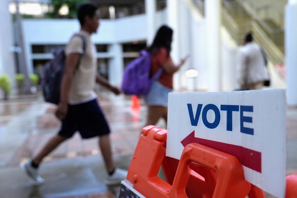 People walk past a "vote" sign.