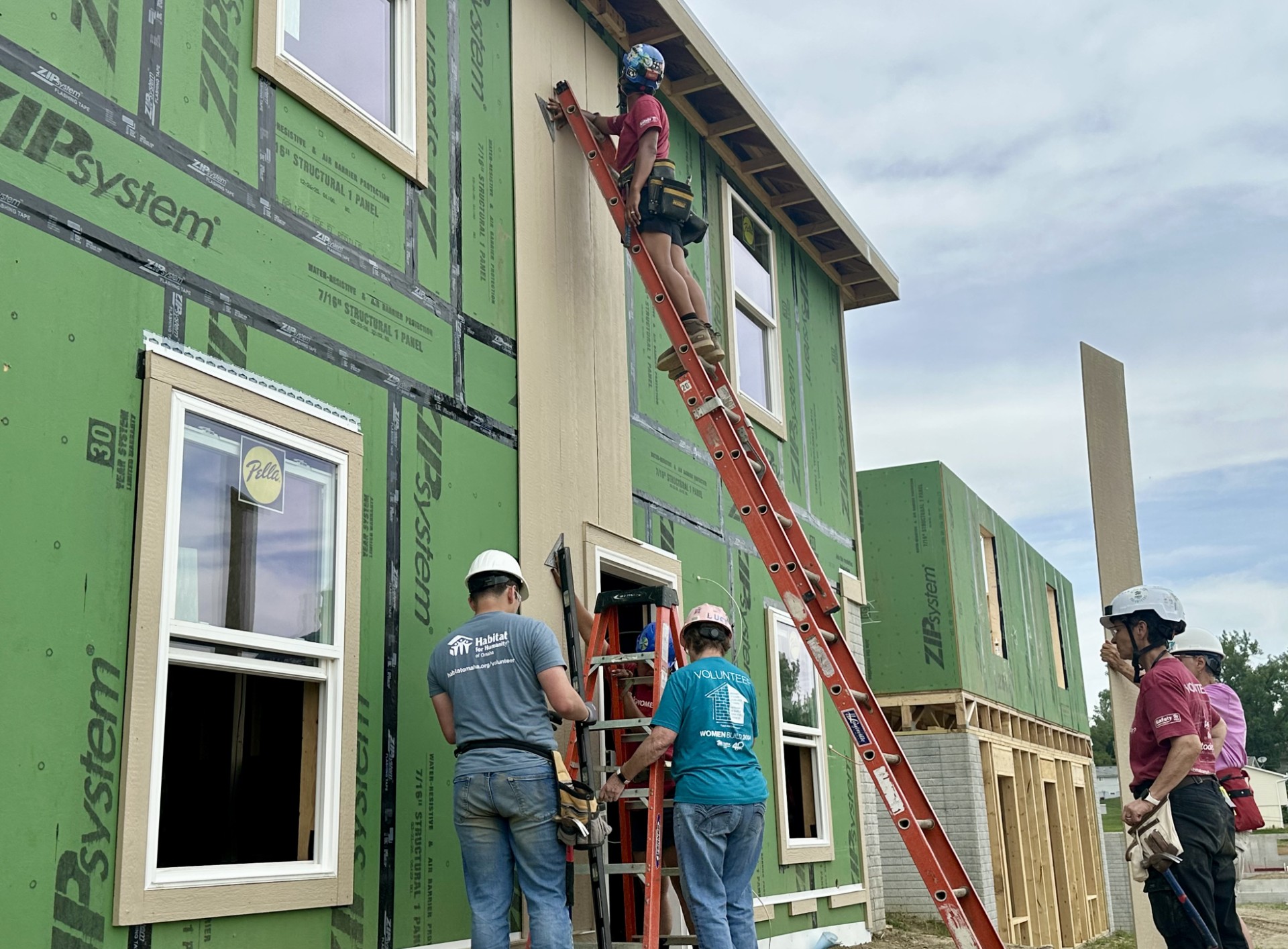 Naveh Bybee, a residential carpenter (lower right), assists volunteers and colleagues on the siding crew.