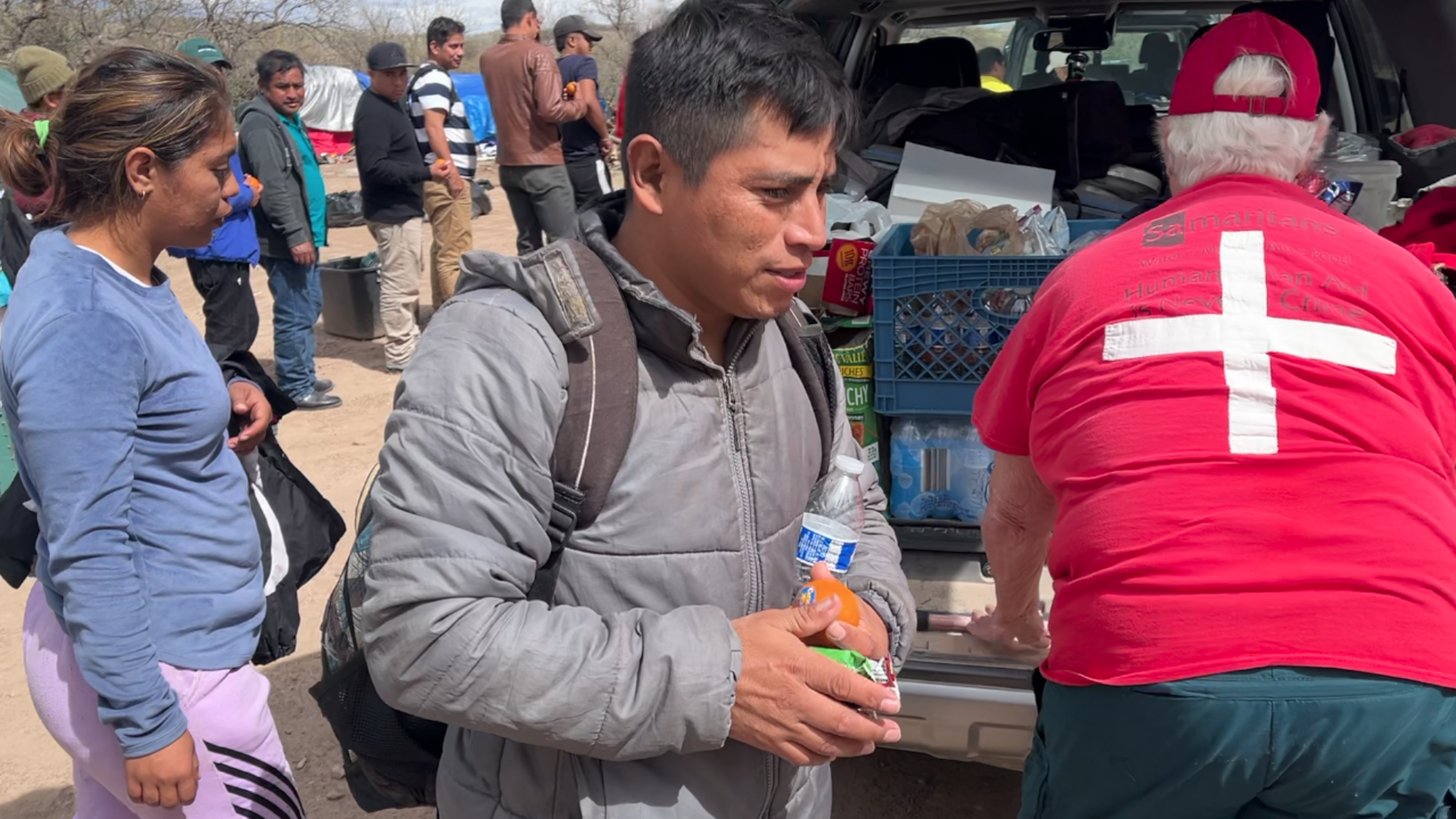 Migrants line up to receive fruit and granola bars from humanitarian aid volunteers near Sasabe, Arizona.