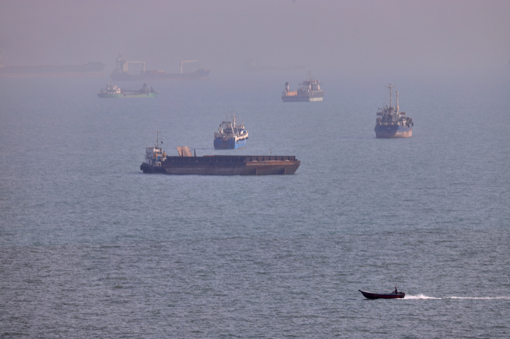A small boat sails past cargo ships and other commercial vessels anchored in the Strait of Hormuz off Bandar Abbas, Iran, Wednesday, Aug. 5, 2026.