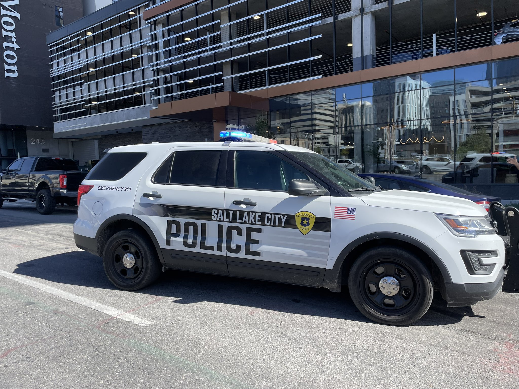 An image of a Salt Lake City Police vehicle is parked in downtown Salt Lake City. It is daytime, and it's lights are flashing.