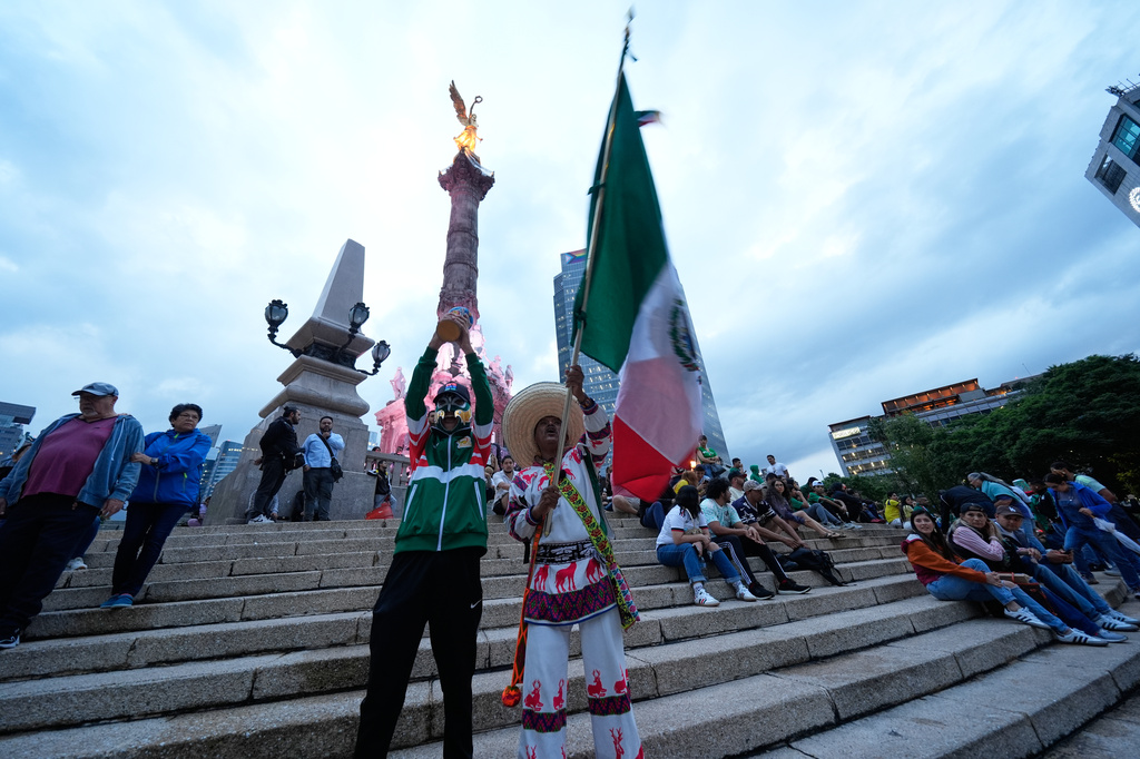 Fans wave a Mexican flag and hold a replica of the FIFA trophy as they gather at the Angel of Independence monument a day before the opening of FIFA World Cup match between Mexico and South Africa in Mexico City, Wednesday, June 10, 2026.