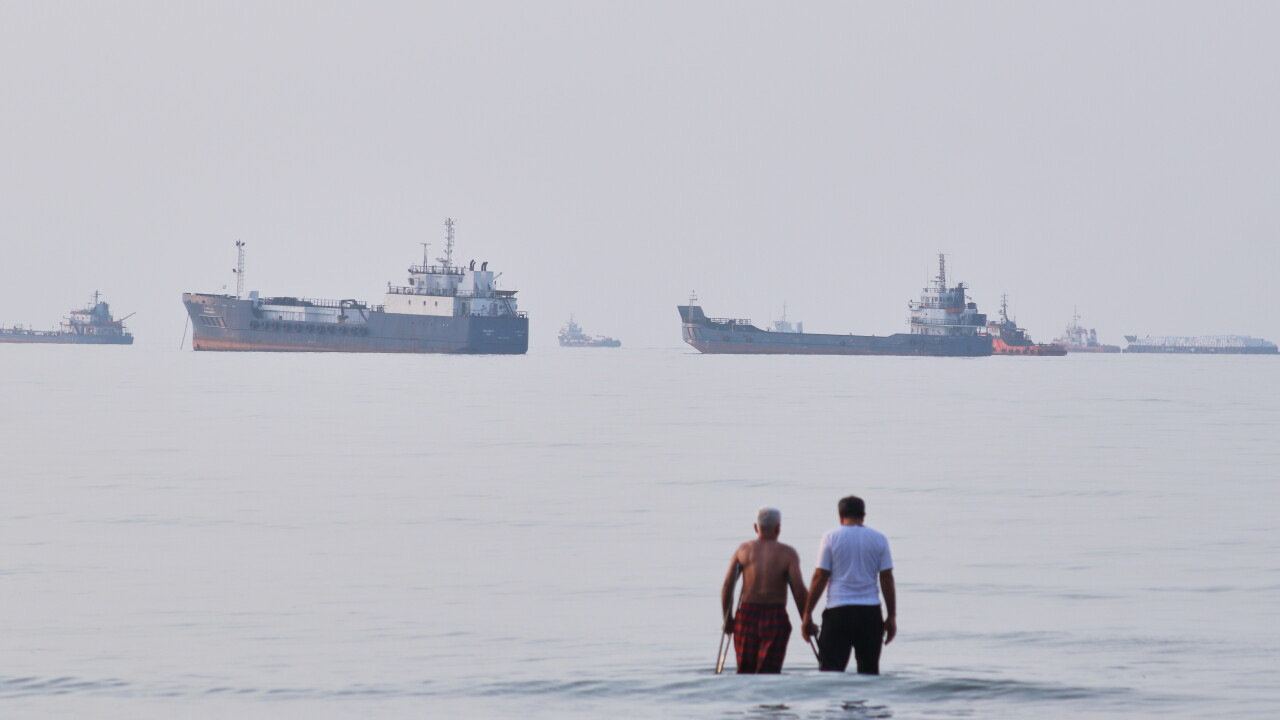 Two men wade in the waters of the Strait of Hormuz with vessels anchored in the background, off Bandar Abbas, Iran, Sunday, July 12, 2026.
