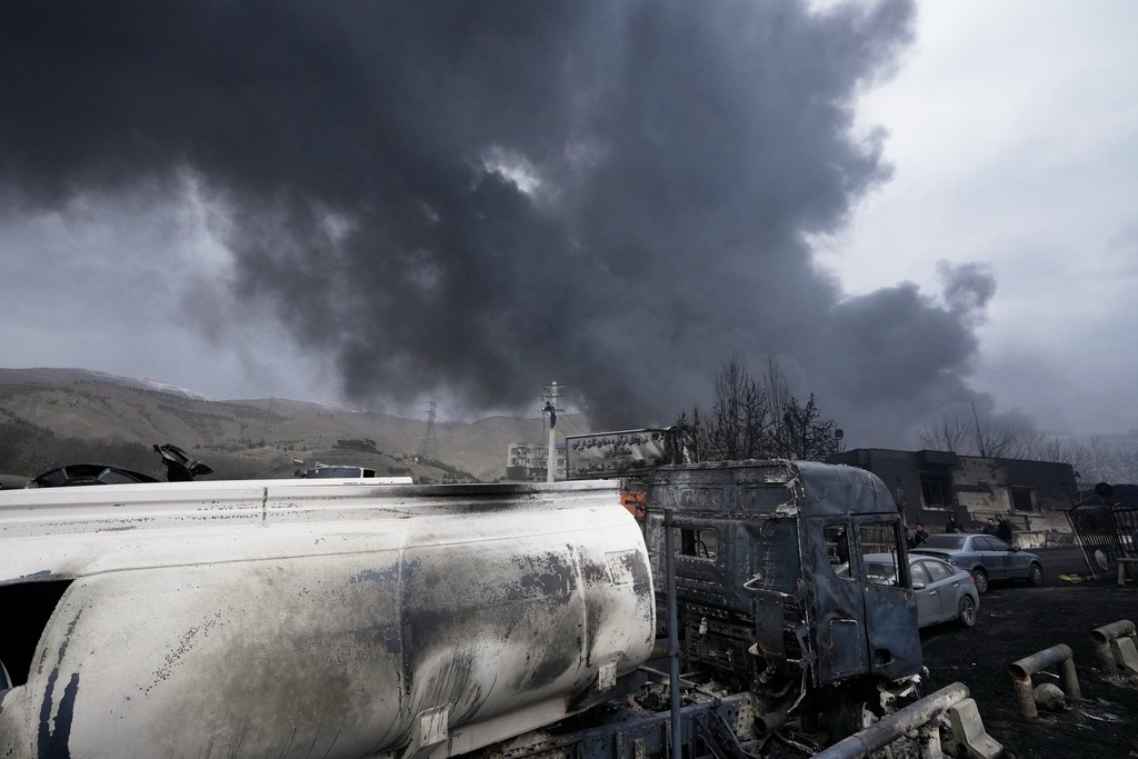 A burned oil tanker truck sits near an oil storage facility struck by a U.S.-Israeli attack late Saturday as a thick plume of smoke rises in Tehran, Iran, Sunday, March 8, 2026.
