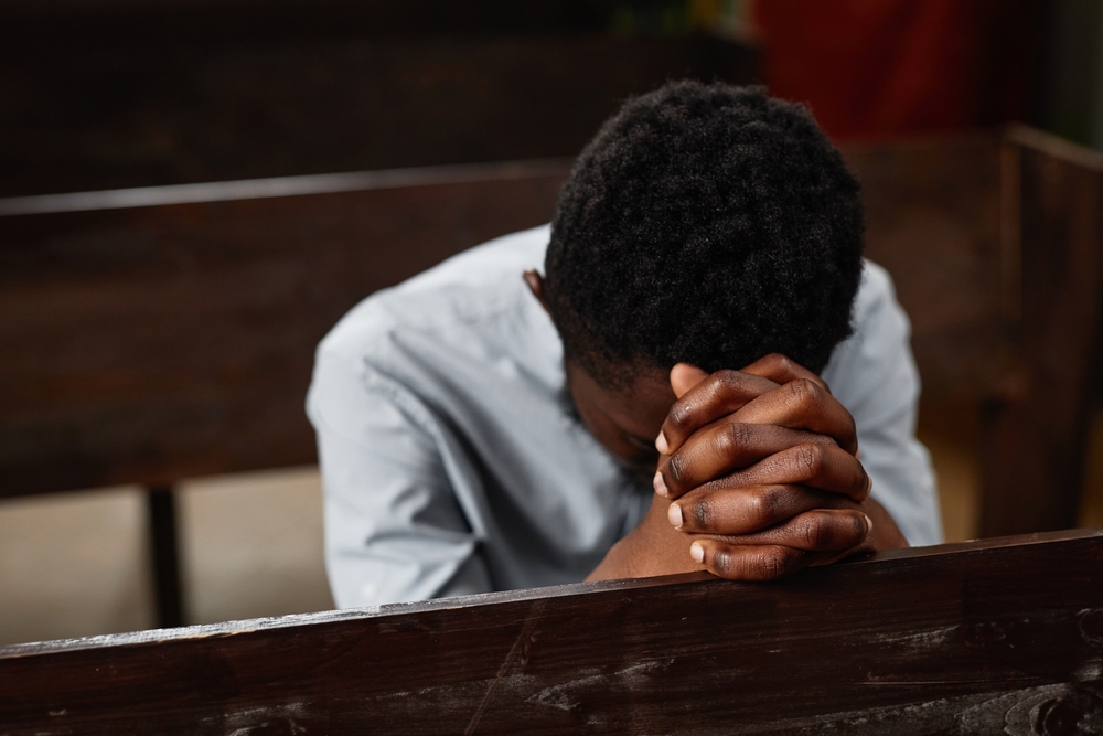 A young man sitting on a bench praying.