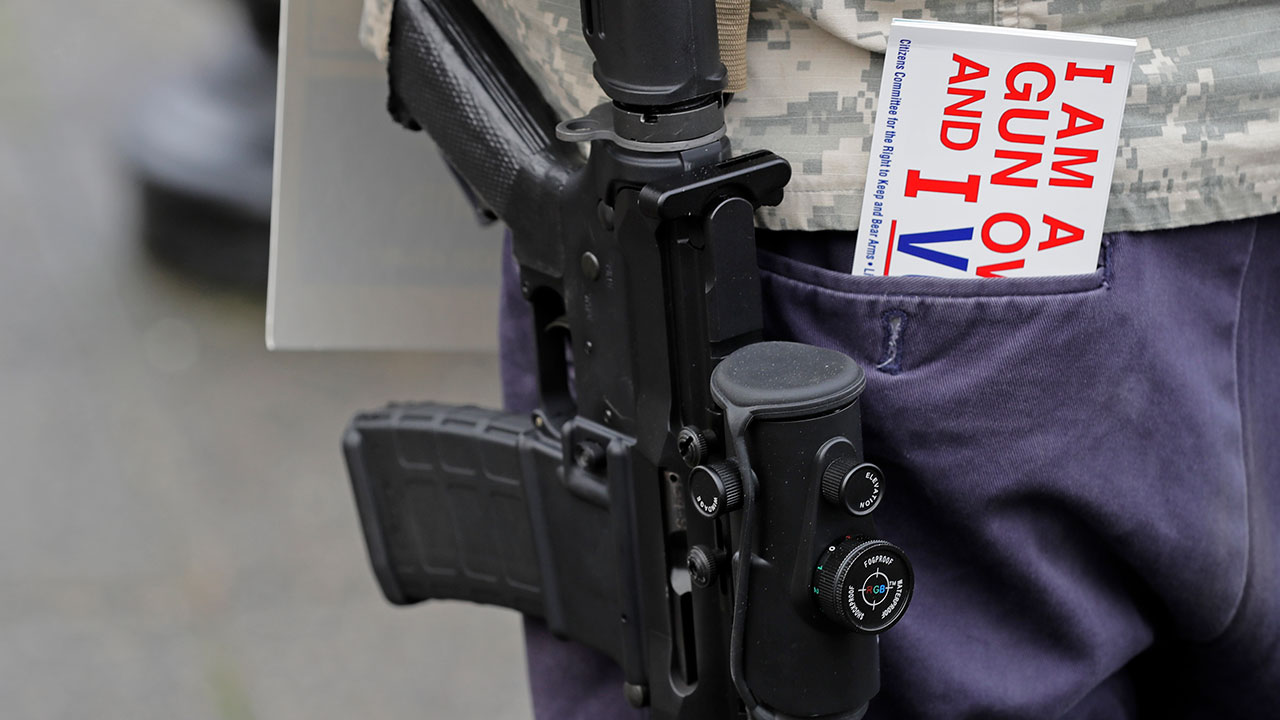 An attendee at a gun-rights rally openly carries a gun next to a bumper sticker that reads "I'm a Gun Owner & I Vote," Friday, Jan. 18, 2019, at the Capitol in Olympia, Wash.