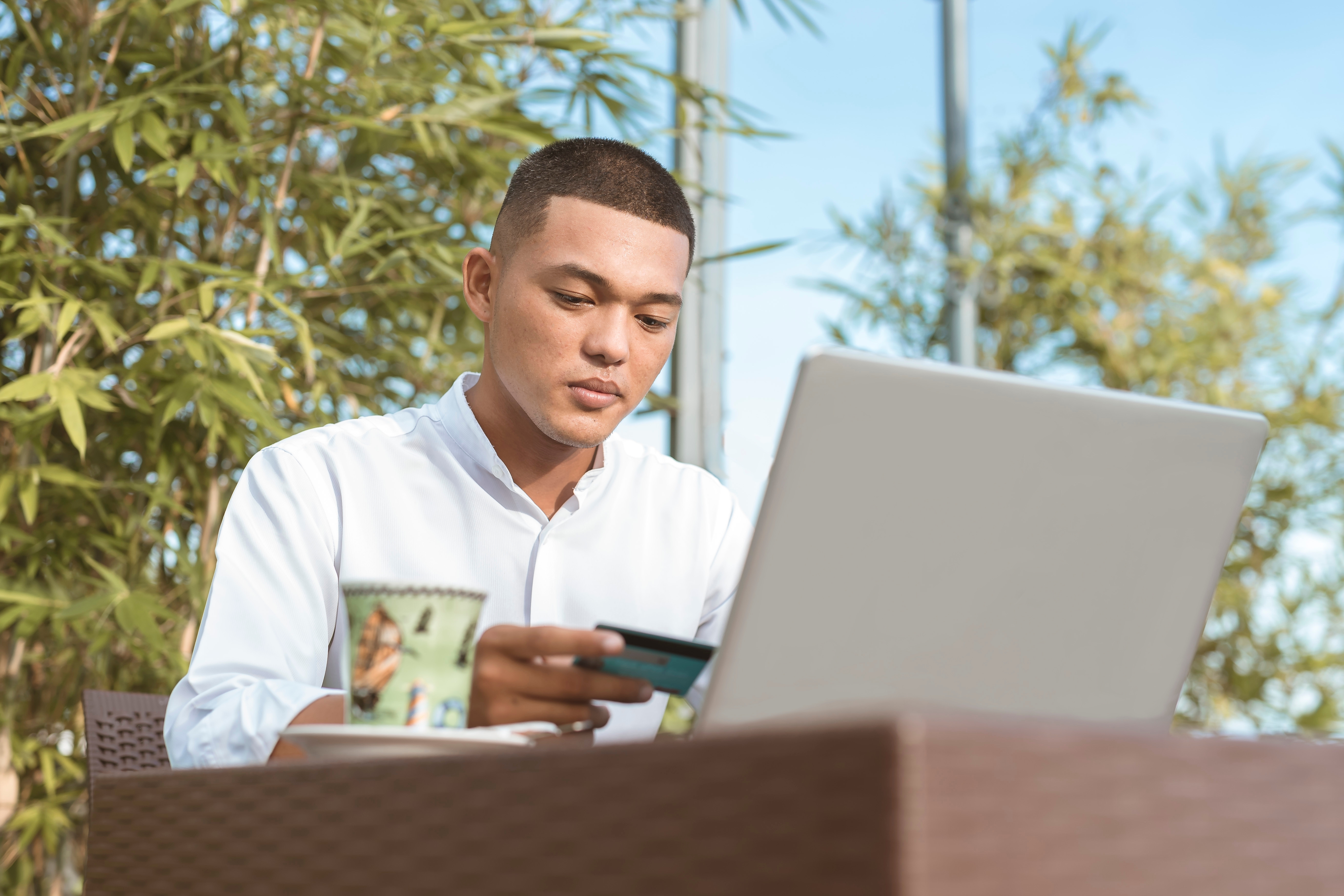 Stock image shows a young man holding a credit card while seated in front of a laptop.