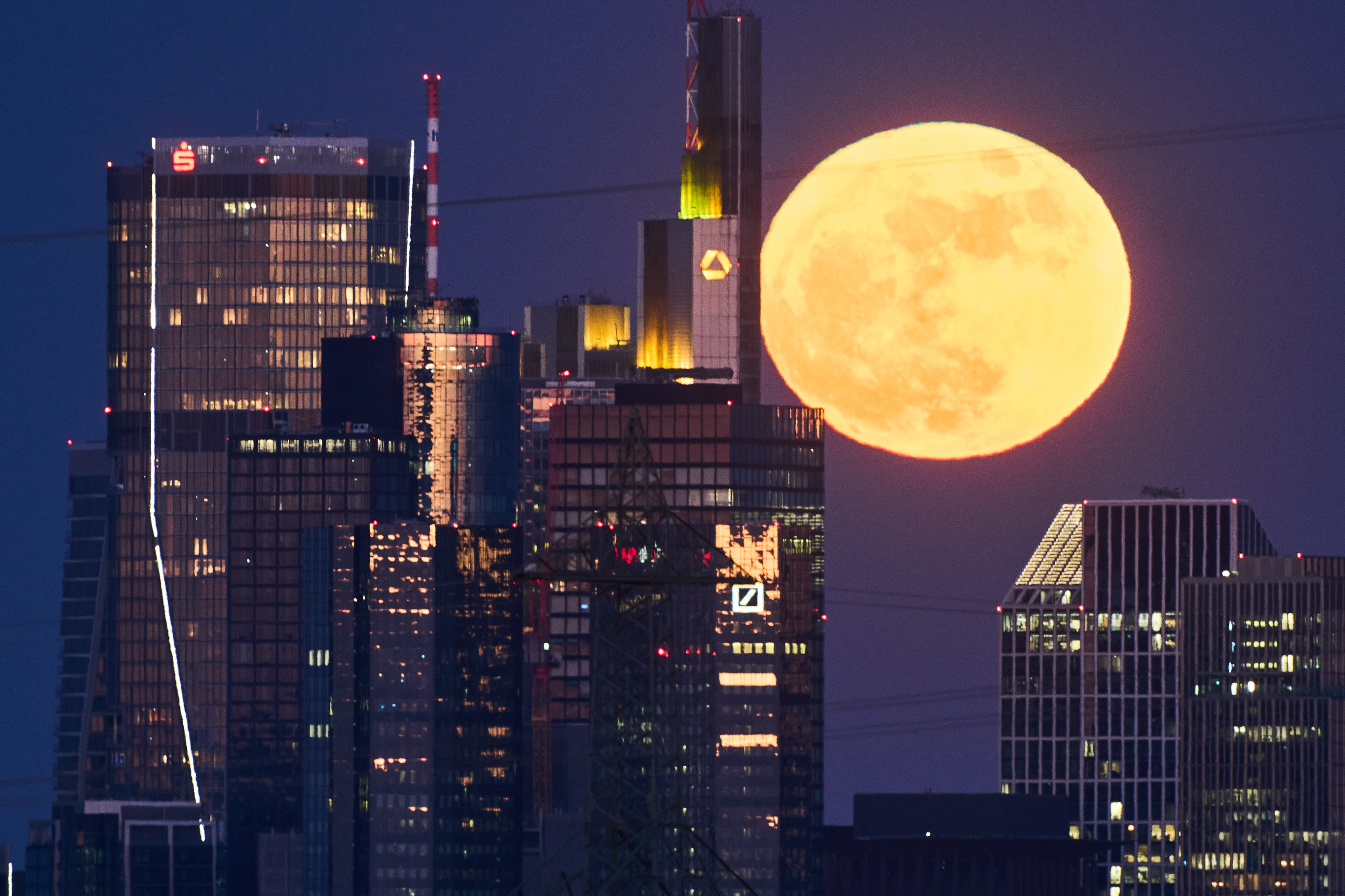 The full moon rises behind the buildings of the banking district in Frankfurt, Germany, Friday, May 1, 2026.